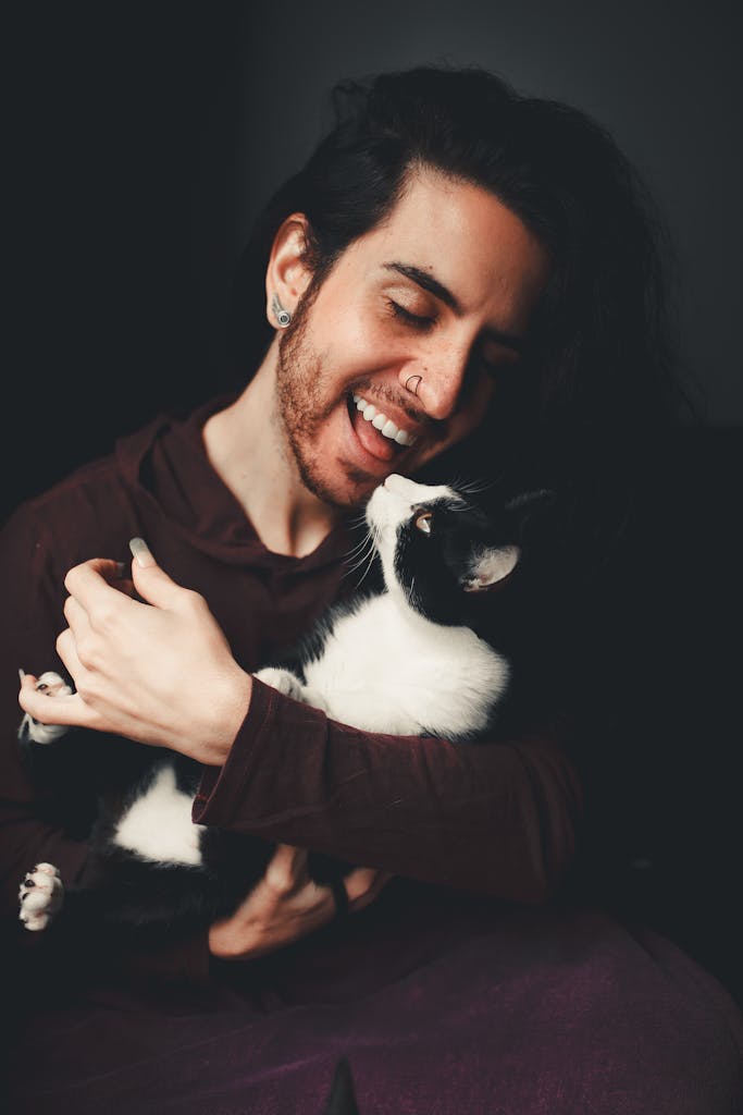 Smiling person cuddling a black and white cat indoors, expressing a joyful bond.